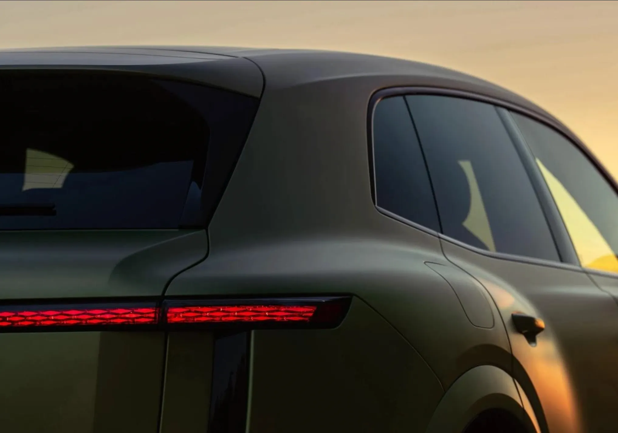 Close-up of the rear of a dark green Bentley Torcal, its full-width red tail light glowing at sunset